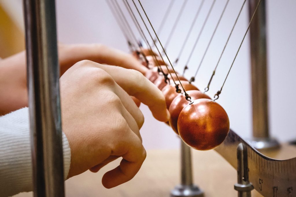 A hand interacts with a Newton's Cradle.