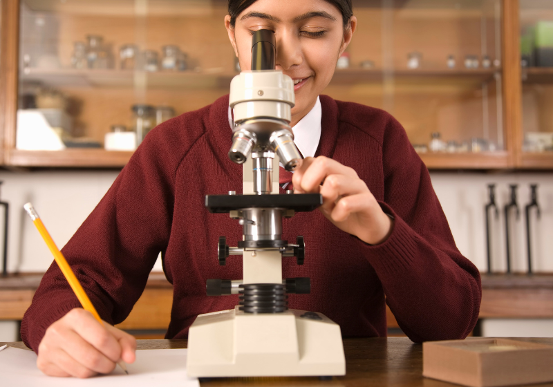 young student looking through a compound microscope